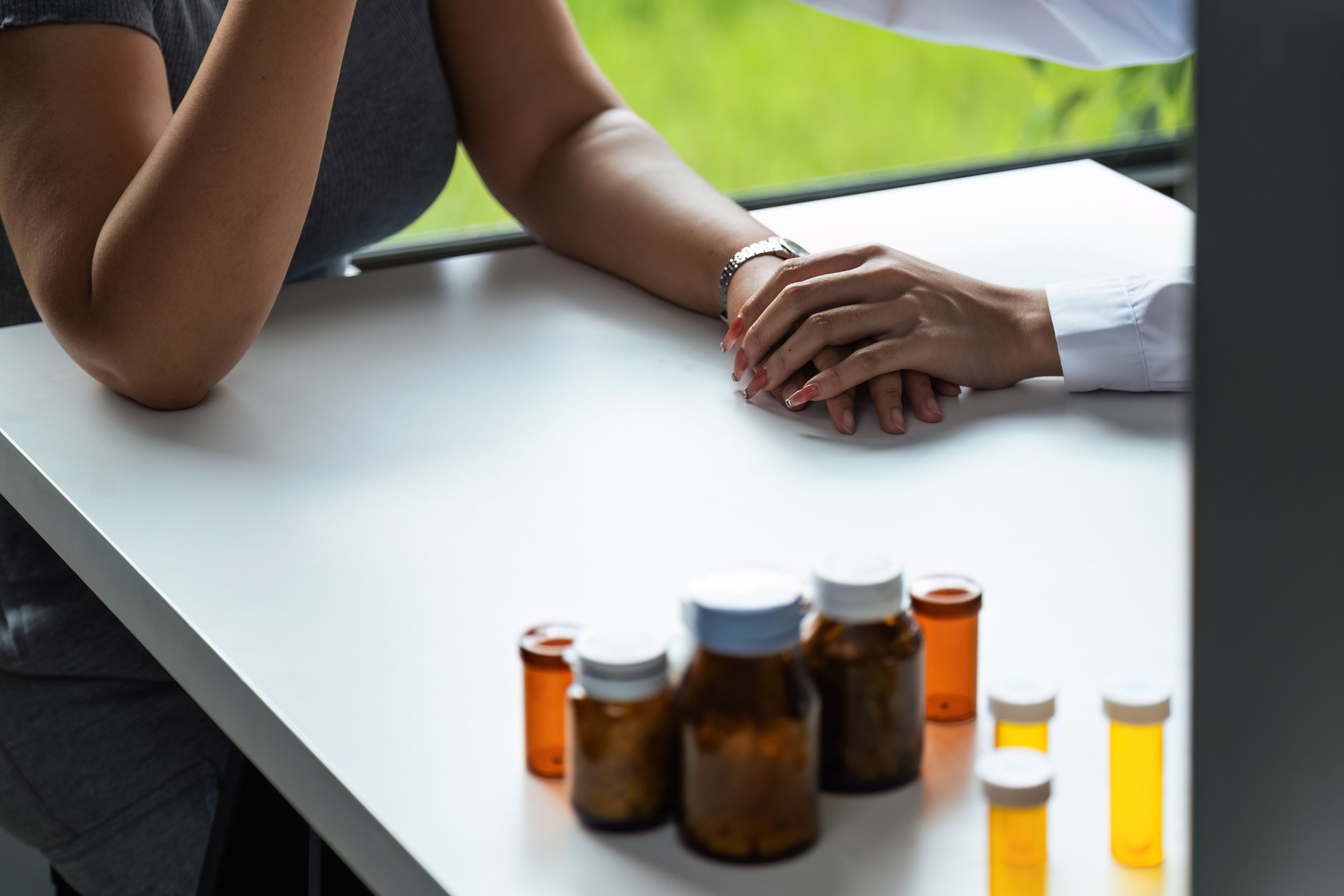 Doctor giving hope. Close up shot of young female physician leaning forward to smiling lady patient holding her hand in palms. Woman caretaker in white coat supporting encouraging old person